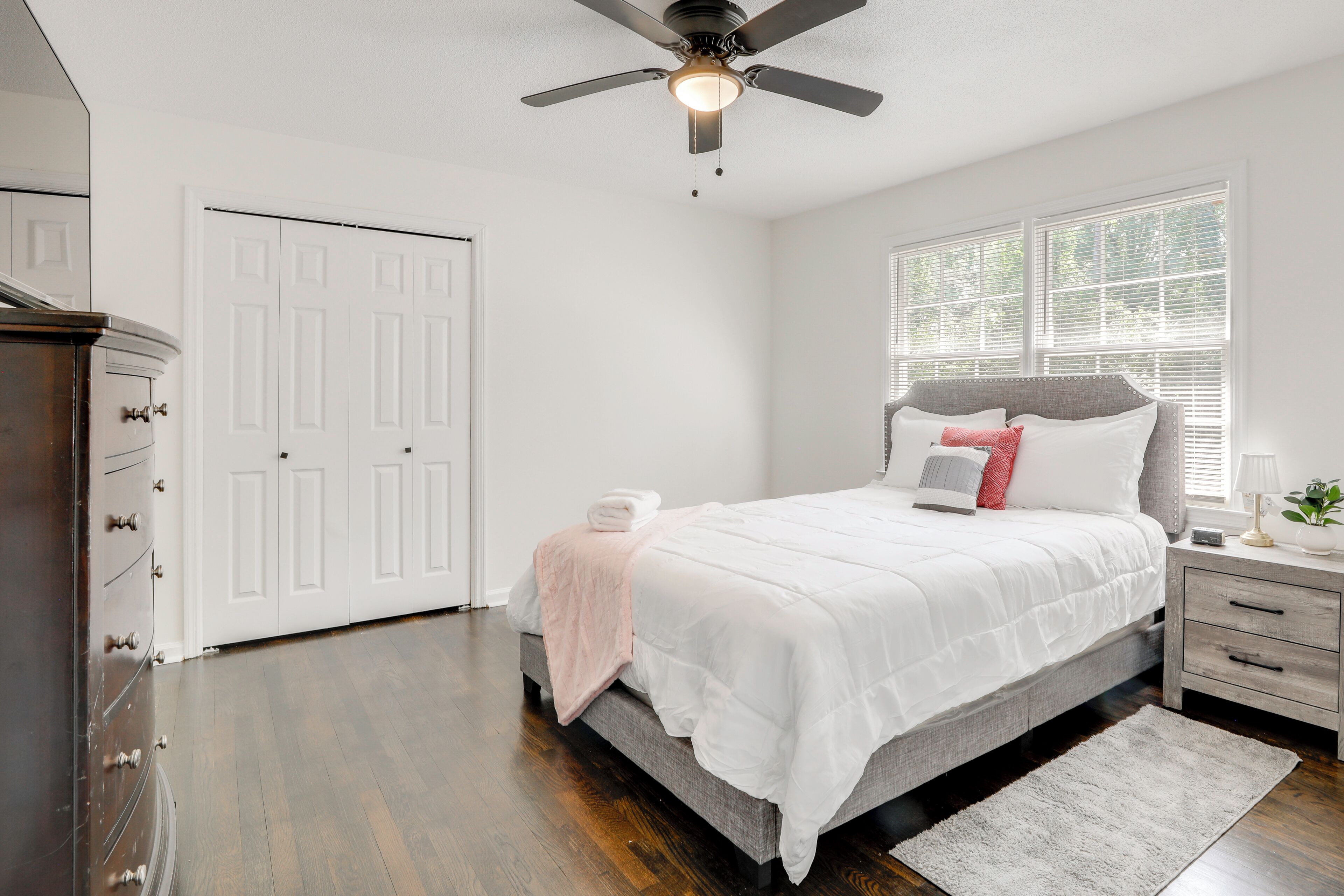 A bedroom with a bed, a nightstand, a dresser, a ceiling fan, and a window with blinds.