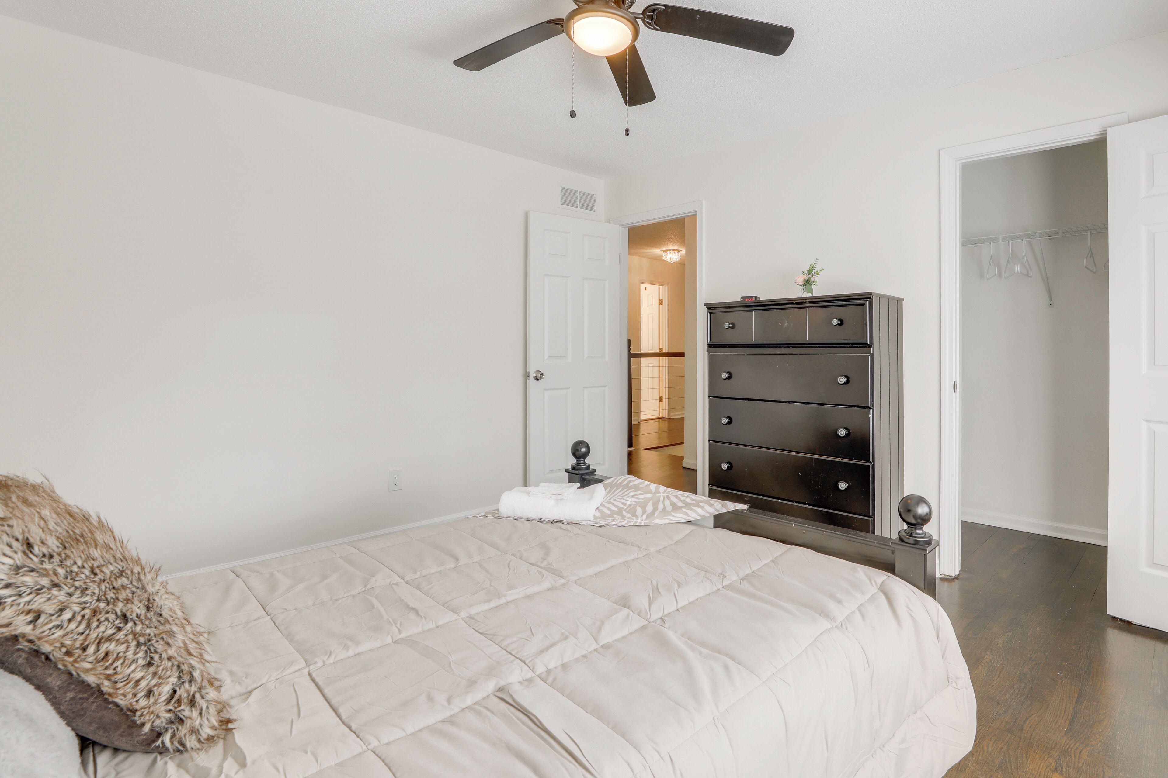 Une chambre à coucher comprenant un lit, un ventilateur de plafond, une commode et une porte donnant sur une autre pièce.