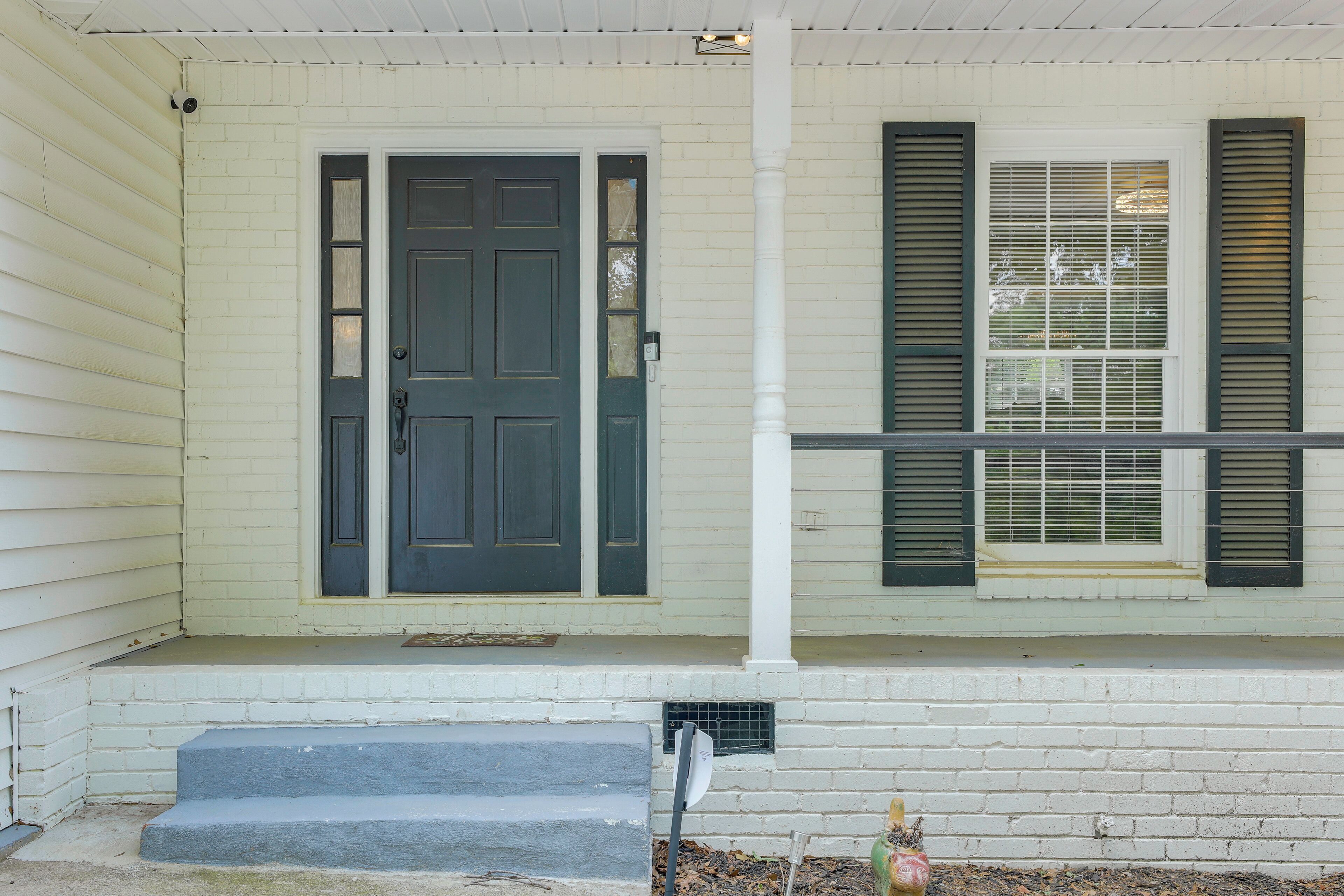 A white house with a dark front door, a small porch, and a window with shutters.