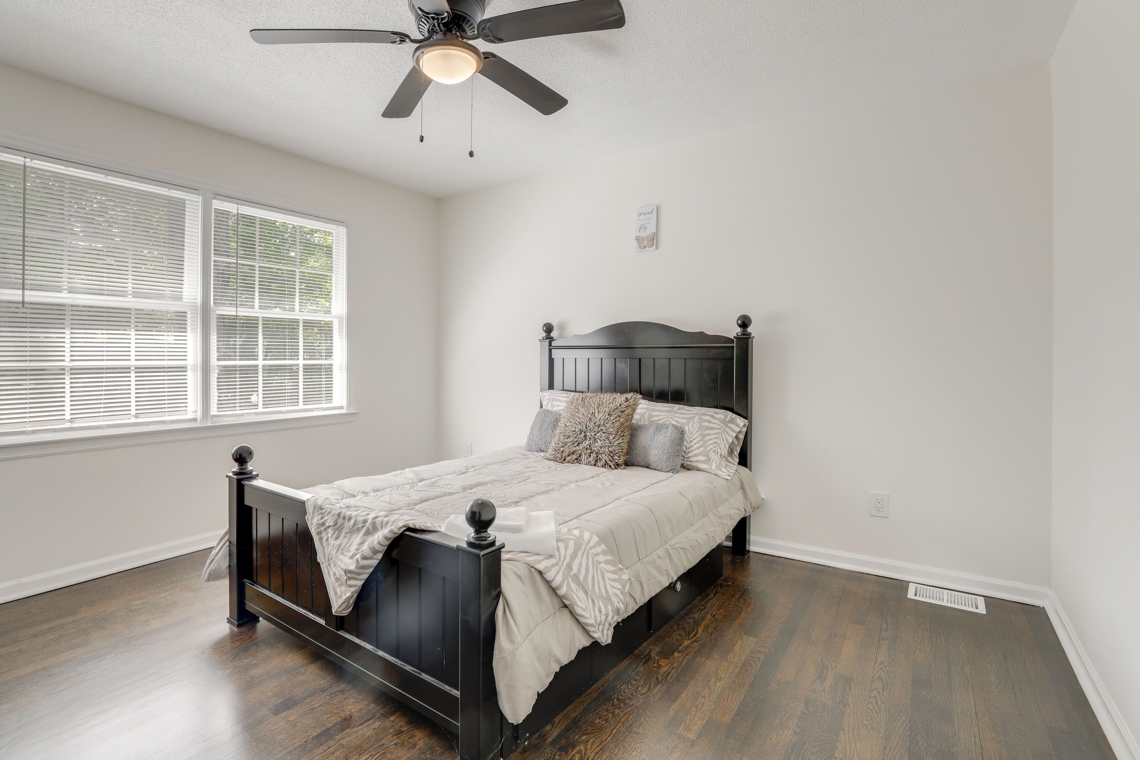 Un dormitorio con cama, ventilador de techo, persianas y una rejilla de ventilación.