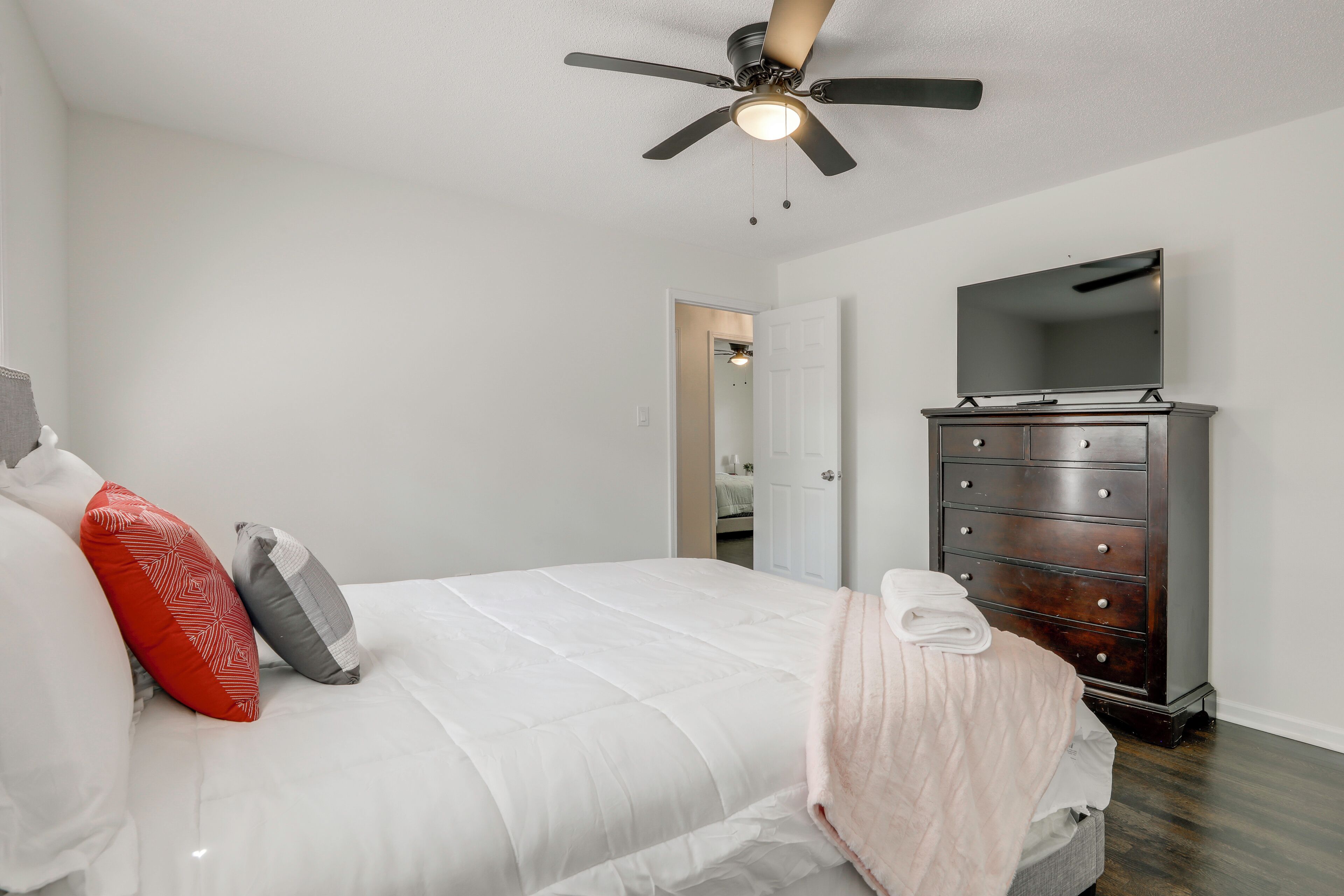 A bedroom with a bed, a dresser, a ceiling fan, and a mirror.