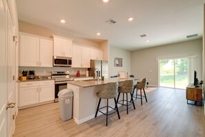 Une cuisine moderne avec des meubles blancs, un îlot central doté de tabourets et une grande fenêtre offrant une vue sur l’extérieur.