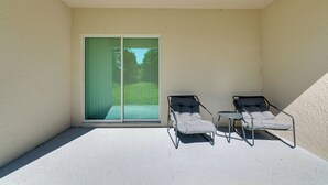 Ein Balkon mit zwei Stühlen und einem kleinen Tisch, eine Schiebeglastür sowie Blick auf eine grüne Rasenfläche.