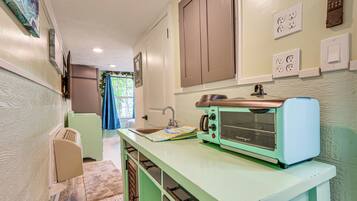 A compact kitchen with a vintage toaster, a sink, and a window with a blue curtain.