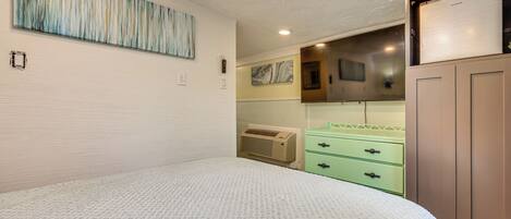 A bedroom with a bed, a green dresser, a wall-mounted air conditioner, and a painting.