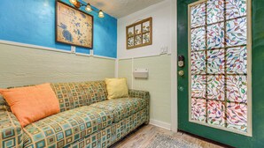A room with a patterned sofa, a green door with a decorative glass panel, and a framed picture on the wall.