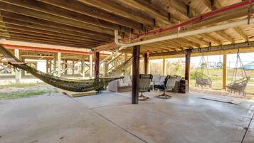 A covered outdoor area with a concrete floor, wooden beams, a hammock, wicker furniture, and a view of the outdoors.