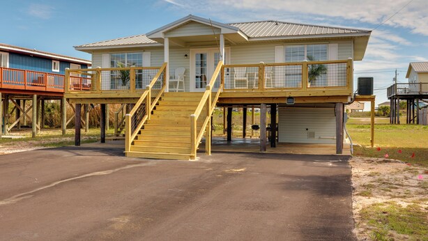 A two-story house with a covered porch, a staircase, and a garage. - Walk to Beach! Waterfront Beach House w/ Deck (Dauphin Island)