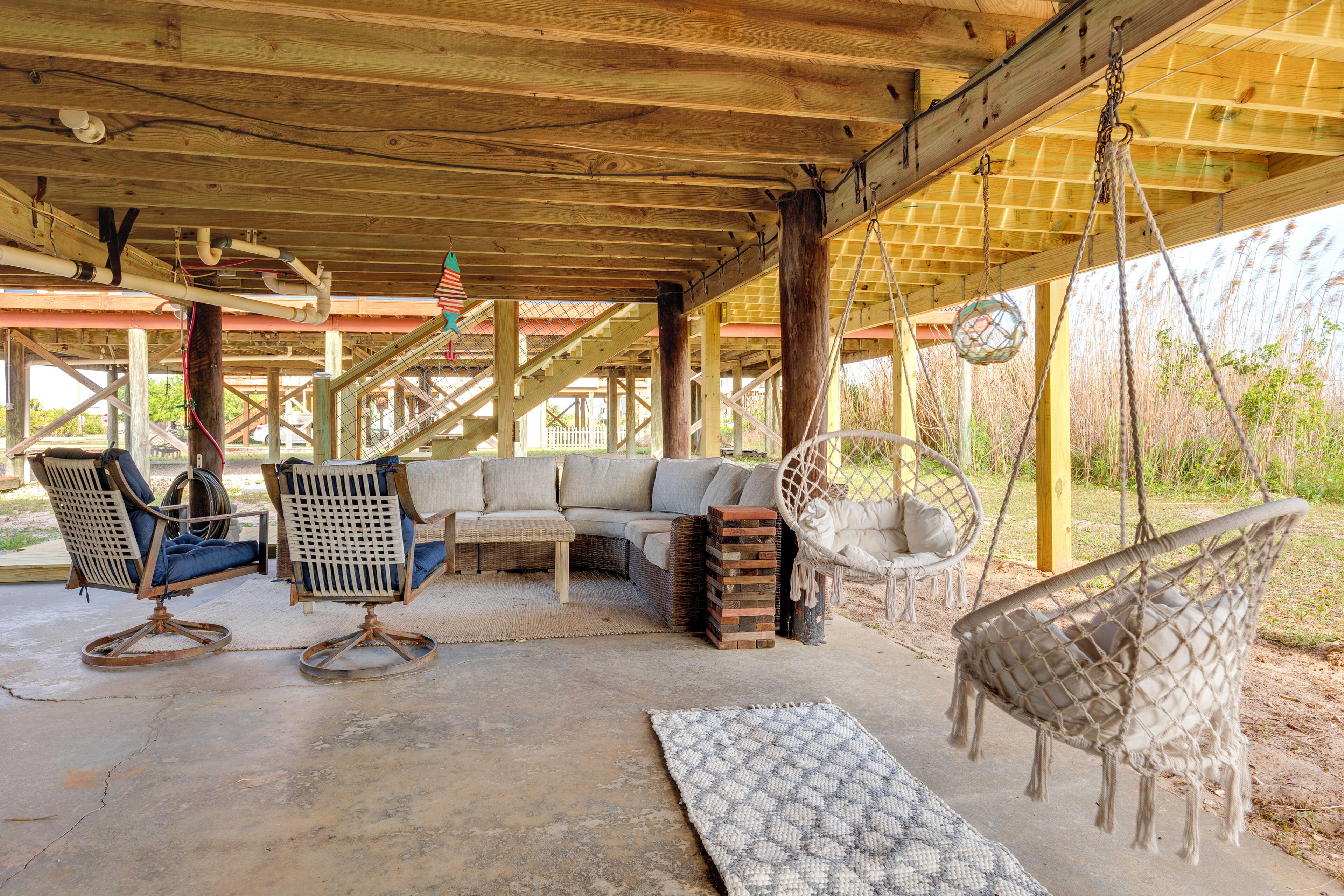 A covered outdoor seating area with a wooden ceiling, a sofa, two rocking chairs, a hanging chair, and a patterned rug.