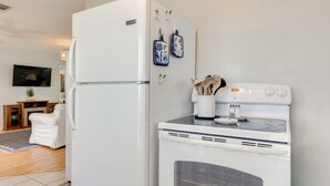 A kitchen with a refrigerator, oven, and microwave. There is a television on the wall and a white chair in the living area. - Walk to Beach! Waterfront Beach House w/ Deck (Dauphin Island)