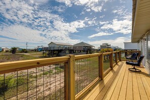 A wooden deck with a railing, a seating area with a table and chairs, and a view of houses in the background. - Walk to Waves! Waterfront Beach House w/ Deck (Dauphin Island)
