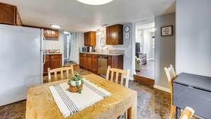 A kitchen with wooden cabinets, a dining table with chairs, and a refrigerator. - Walk to Park, Trails & Pub! Palmer Lake Cottage (Palmer Lake)
