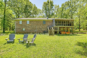 A rustic cabin with a brick exterior, a deck, and two Adirondack chairs in a grassy area.