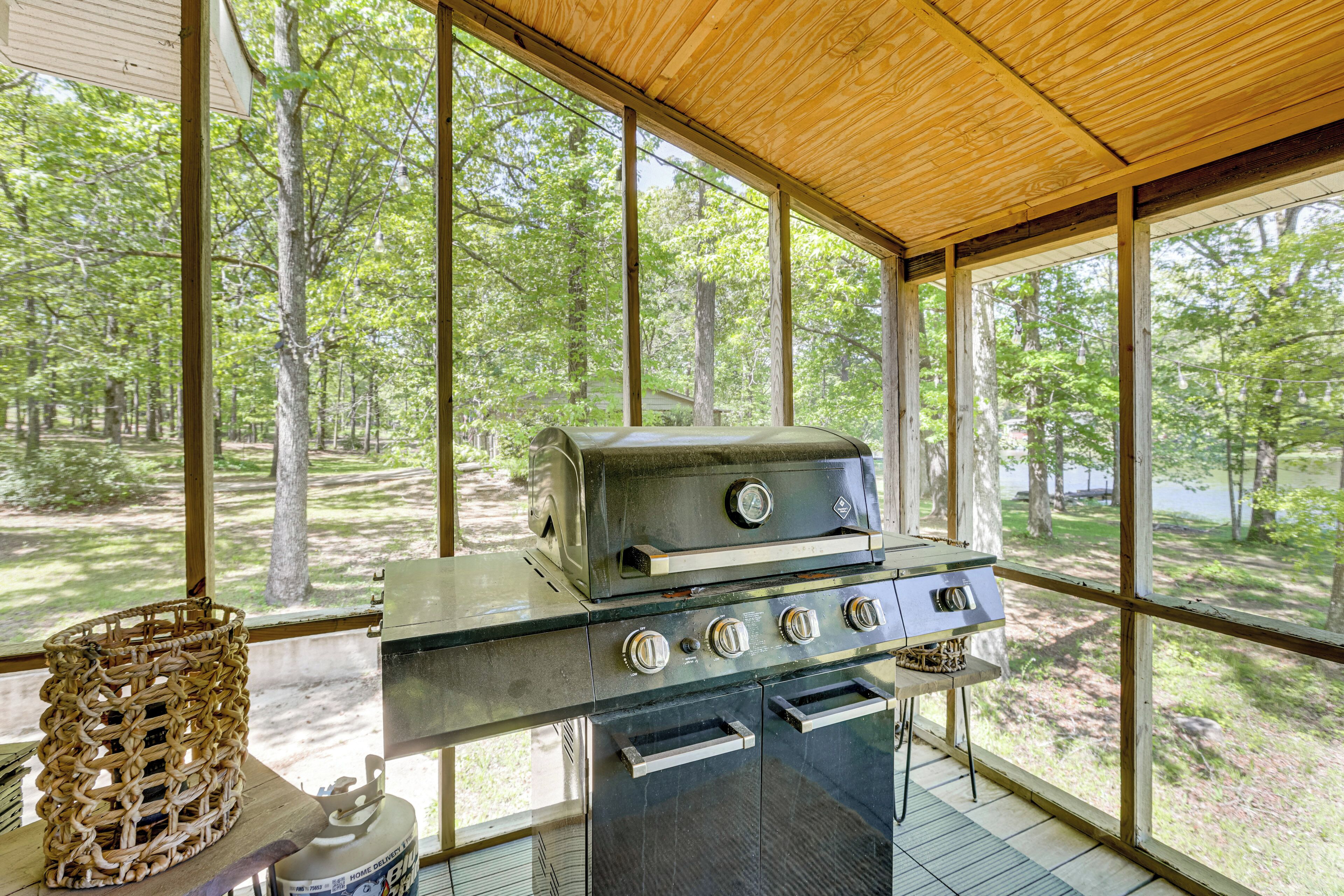Eine überdachte Außenküche mit Grill, Korb und Blick auf einen Wald.