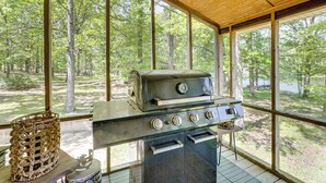 Une cuisine extérieure abritée, équipée d’un barbecue, d’un panier et offrant une vue sur une forêt.