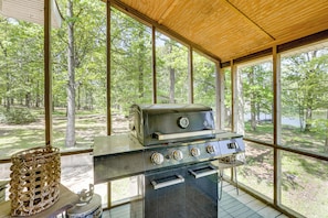 A covered outdoor kitchen with a grill, a basket, and a view of a forest.