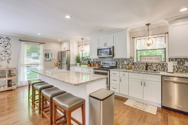 A modern kitchen with white cabinetry, a central island with bar stools, stainless steel appliances, and a view of the outdoors.