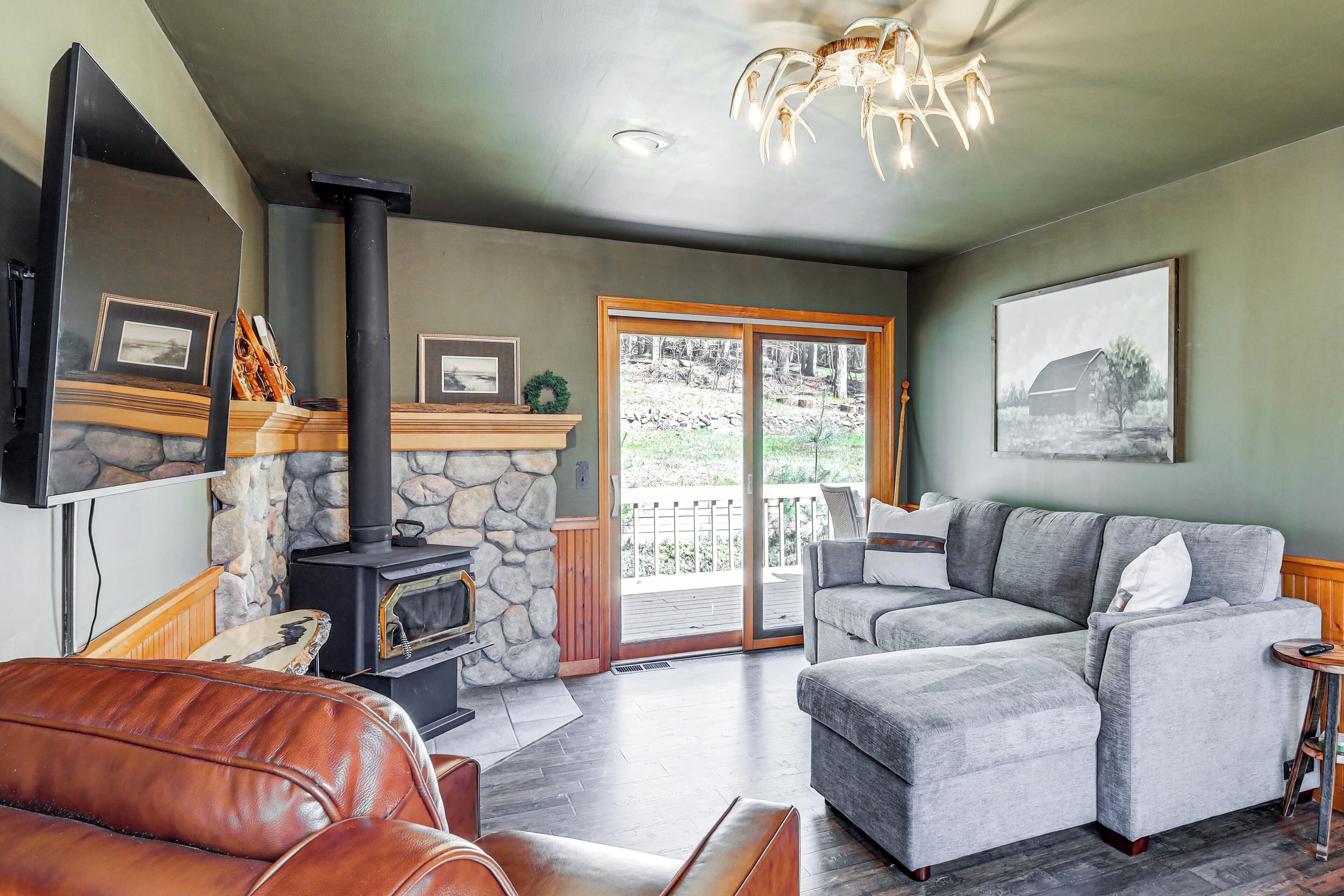 A living room with a stone fireplace, a grey sectional sofa, a leather couch, and a television mounted on the wall.
