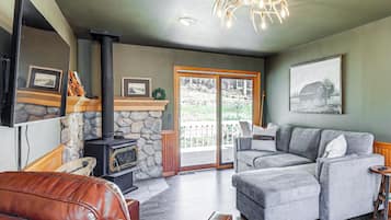 A living room with a stone fireplace, a grey sectional sofa, a leather couch, and a television mounted on the wall.