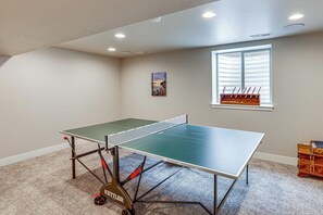 A ping pong table in a room with a window, carpeted floor, and a small wooden chest. - Next to Public Golf Course! Kalispell Townhome (Kalispell)