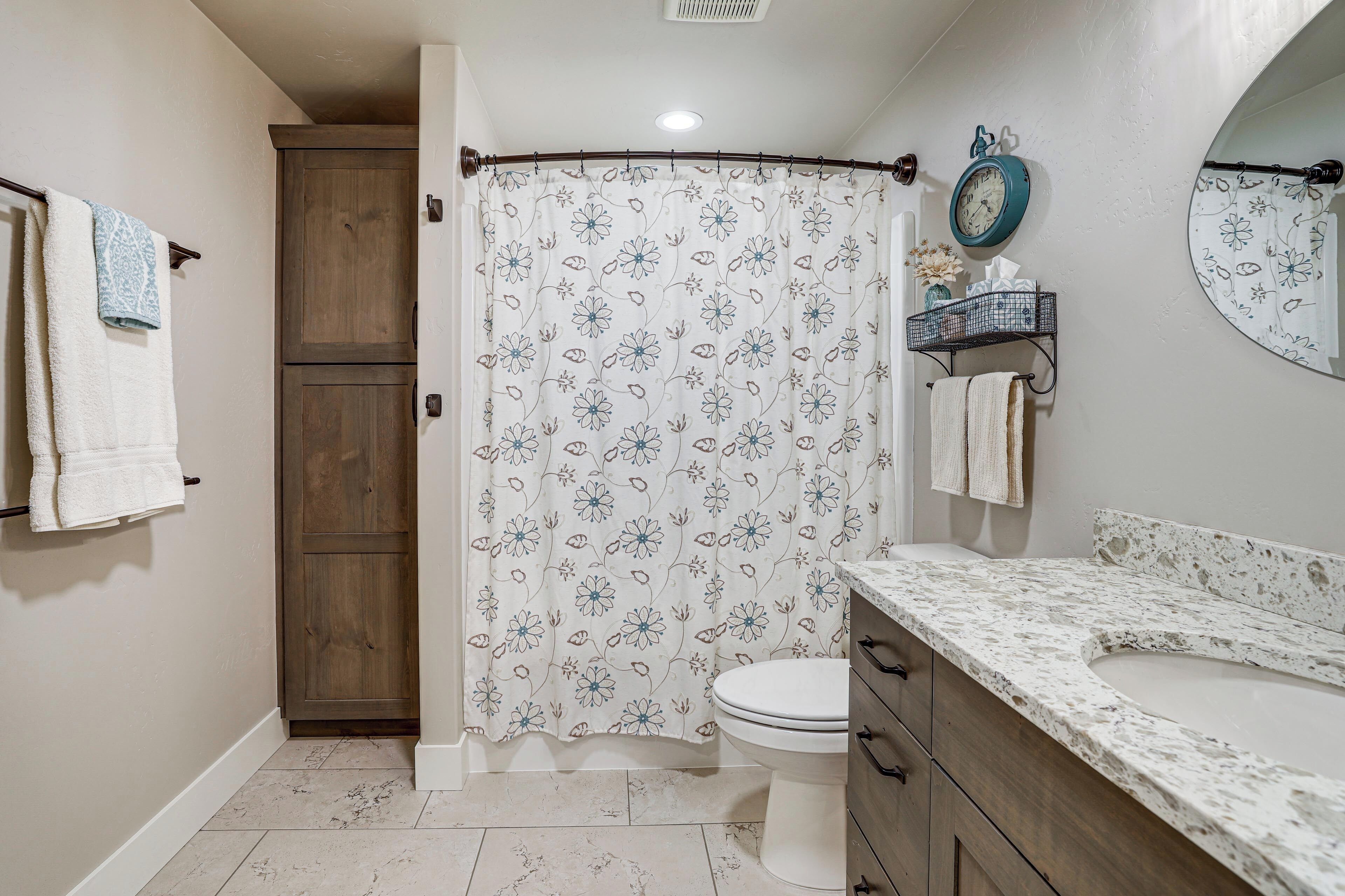 Un baño con cortina de ducha, inodoro, lavamanos con encimera de mármol y un mueble de madera.