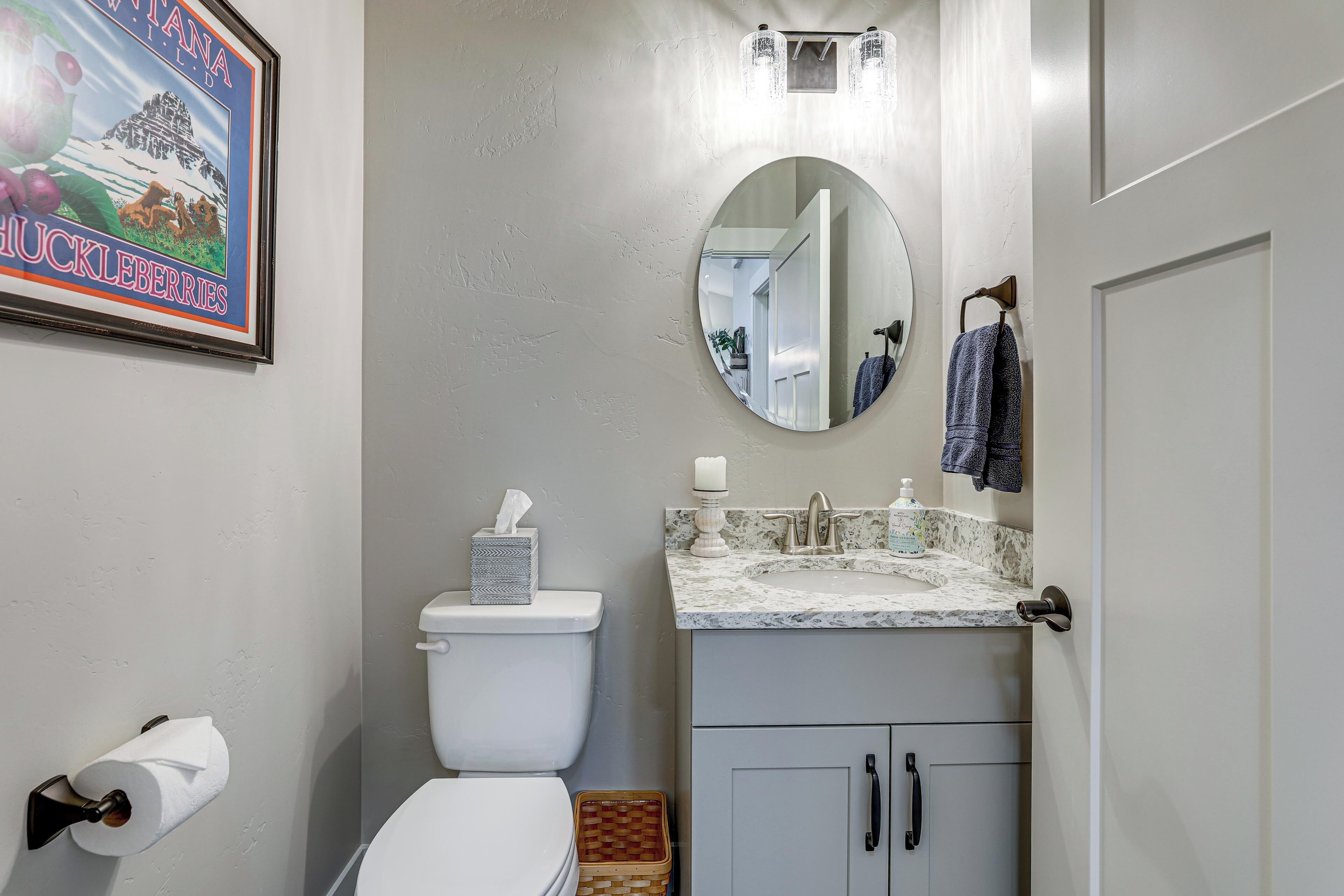 Une salle de bain équipée de toilettes, d’un lavabo, d’un miroir et d’un tableau représentant un paysage où l’on voit des myrtilles.