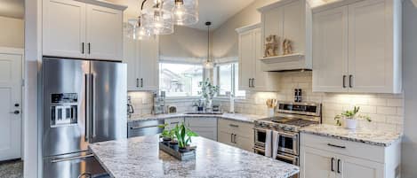 A modern kitchen with stainless steel appliances, white cabinetry, granite countertops, and pendant lighting.
