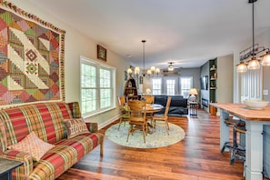 A cozy living room with a plaid sofa, a dining table with chairs, a large rug, and a kitchen area with a bar. - Home on Lake Hartwell! Dock, Decks & Endless Fun (Toccoa)