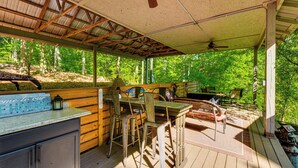 Un espace extérieur abrité, doté d’une table et de chaises en bois, d’un comptoir de bar et offrant une vue sur la forêt.