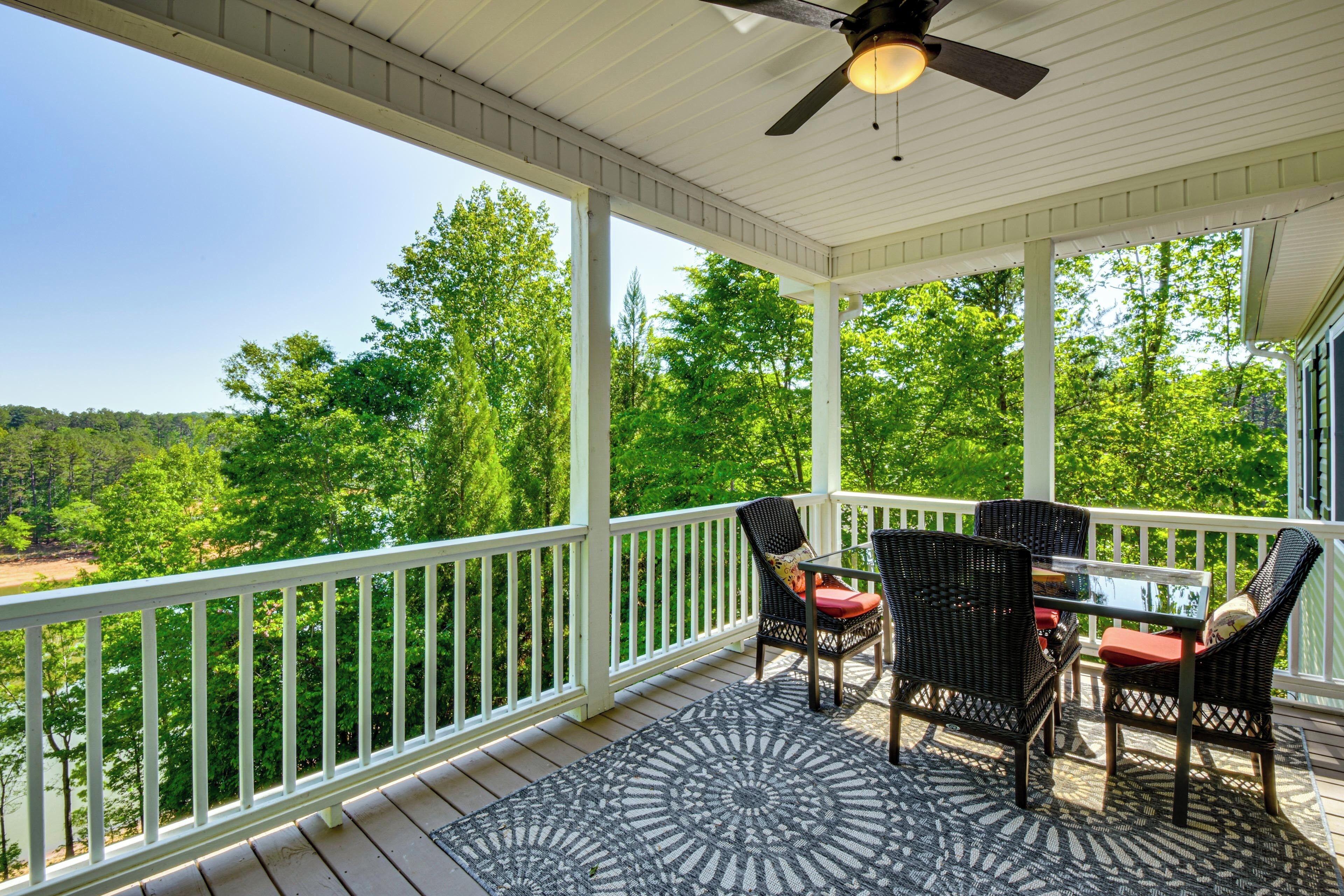 A covered outdoor area with a table and chairs, a ceiling fan, and a view of a forested landscape.
