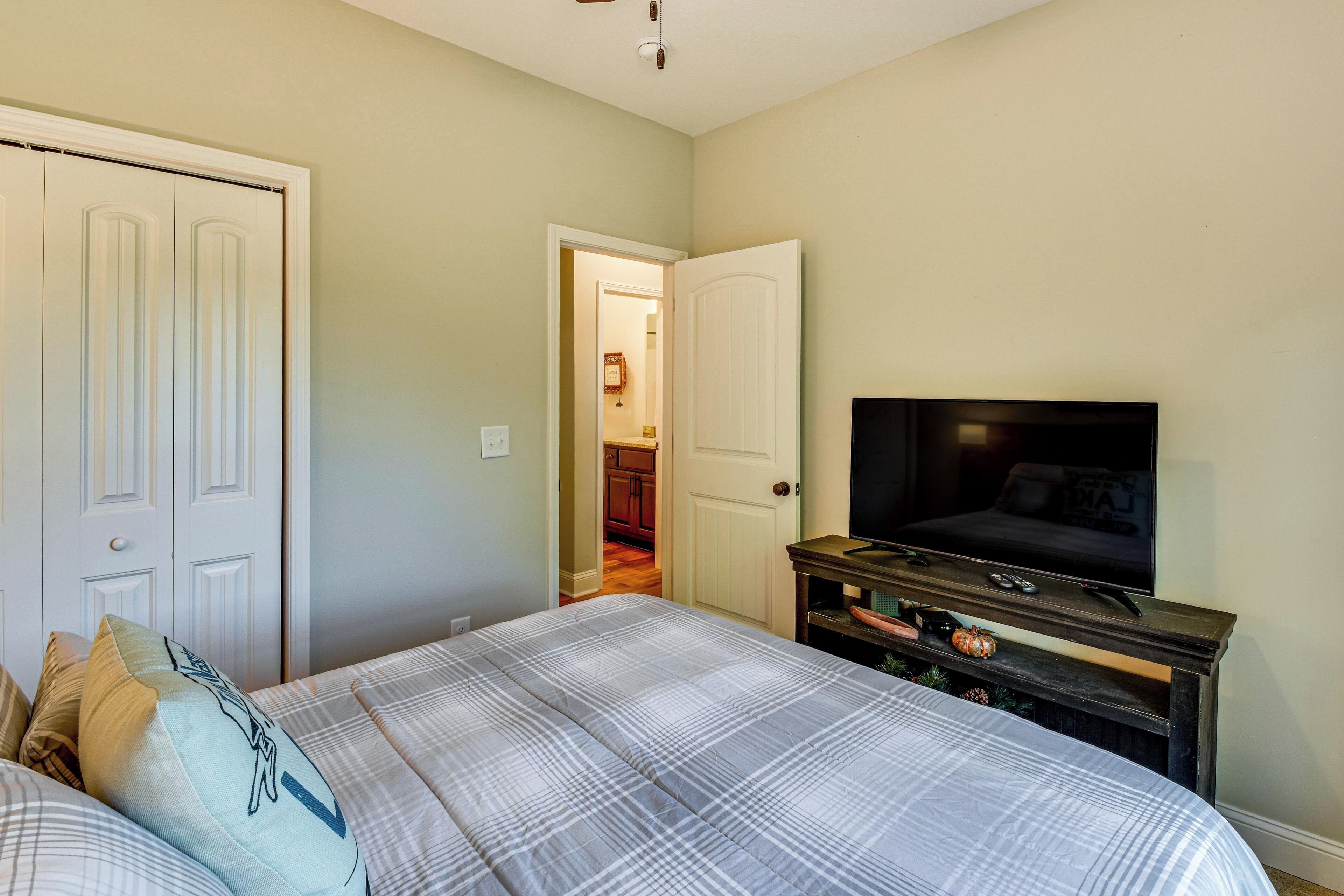 A bedroom with a bed, a television on a stand, and a door leading to a bathroom.