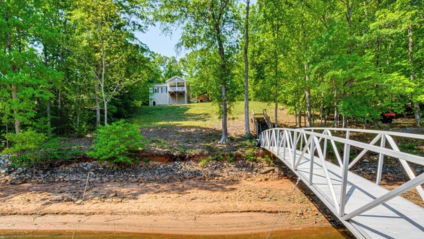 Un pont en bois enjambant une rivière, entouré d’arbres, avec une maison en arrière-plan.