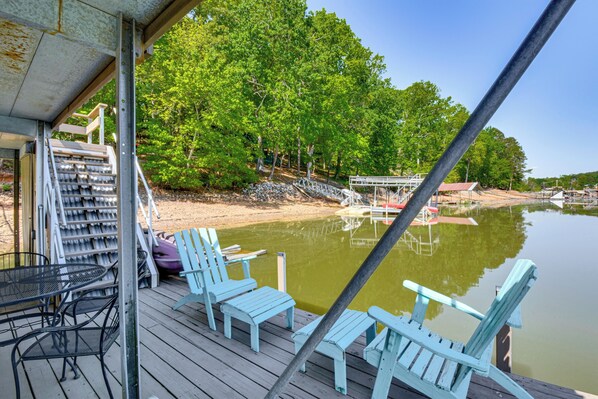 A wooden deck with chairs and a table, overlooking a calm lake with boats and trees.