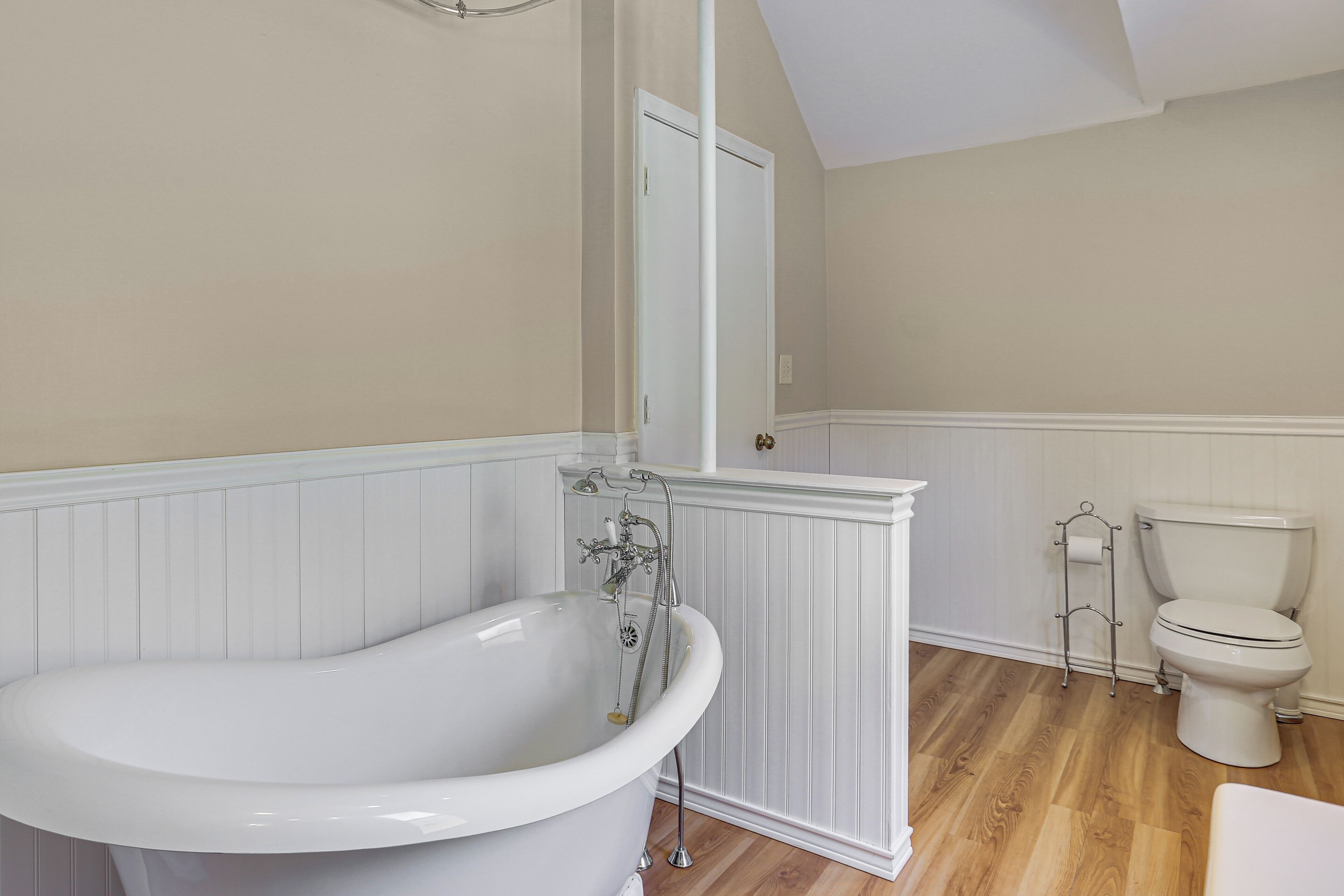 A bathroom with a freestanding bathtub, a toilet, and a white door.