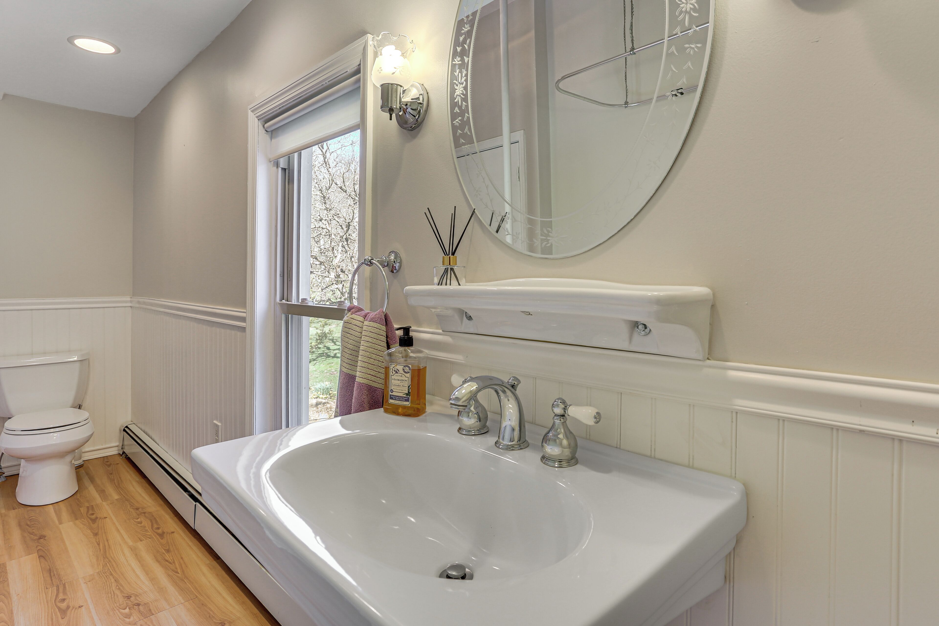 A bathroom with a white sink, two faucets, a mirror, a window, and a toilet.