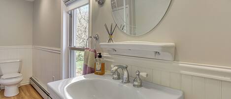 A bathroom with a white sink, two faucets, a mirror, a window, and a toilet.