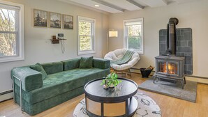 A cozy living room with a green sofa, a round table with a plant, a fireplace, and artwork on the walls.