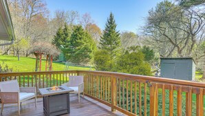 A wooden deck with a table and chairs, surrounded by a wooden railing, overlooking a grassy yard with trees and a shed.