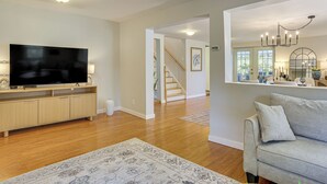 A living room with a flat-screen TV, a grey sofa, wooden flooring, and a staircase leading to another room.
