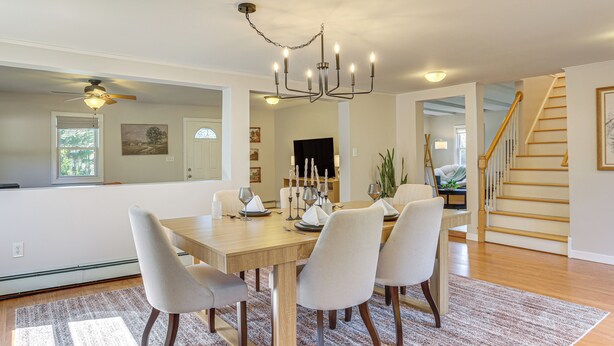 A dining area with a wooden table, six chairs, a chandelier, and a staircase in the background.