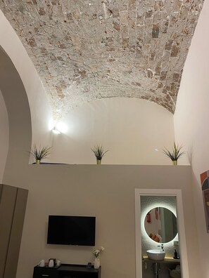 A room with a brick ceiling, a flat-screen TV, a round mirror, and a sink. - WITHIN WALKING DISTANCE OF CENTRAL STATION AND NAPLES BUSINESS CENTER. (Napoli)