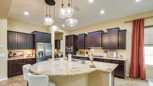 Una cocina con alacenas de madera oscura, una isla de granito e iluminación colgante.