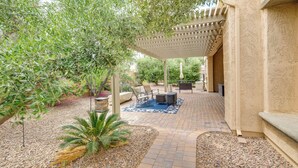 Un patio al aire libre con una pérgola, mobiliario y una planta de palma.