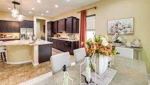 Una cocina moderna con armarios oscuros, una isla central y una zona de comedor con mesa y sillas.