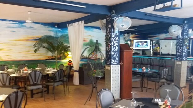 A restaurant with indoor seating, a mural of a sunset over water, and a bar area. - Fana Hotel (Dakar)