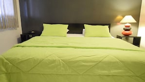 A bed with a green bedspread and pillows, a nightstand with a lamp, and a dark headboard. - Fana Hotel (Dakar)