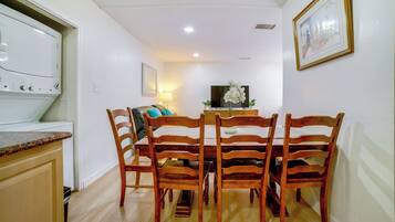 Uma sala de jantar com mesa e cadeiras de madeira, uma televisão e uma cozinha com fogão.
