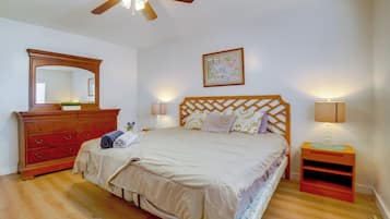 Quarto com cama, penteadeira, mesa de cabeceira, abajur, ventilador de teto e um quadro na parede.
