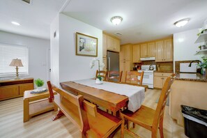 A dining area with a wooden table and benches, a kitchen with wooden cabinets, and a small plant on the windowsill. - Family-friendly Home 7 Mi to Dtwn San Bernardino! (Rialto)