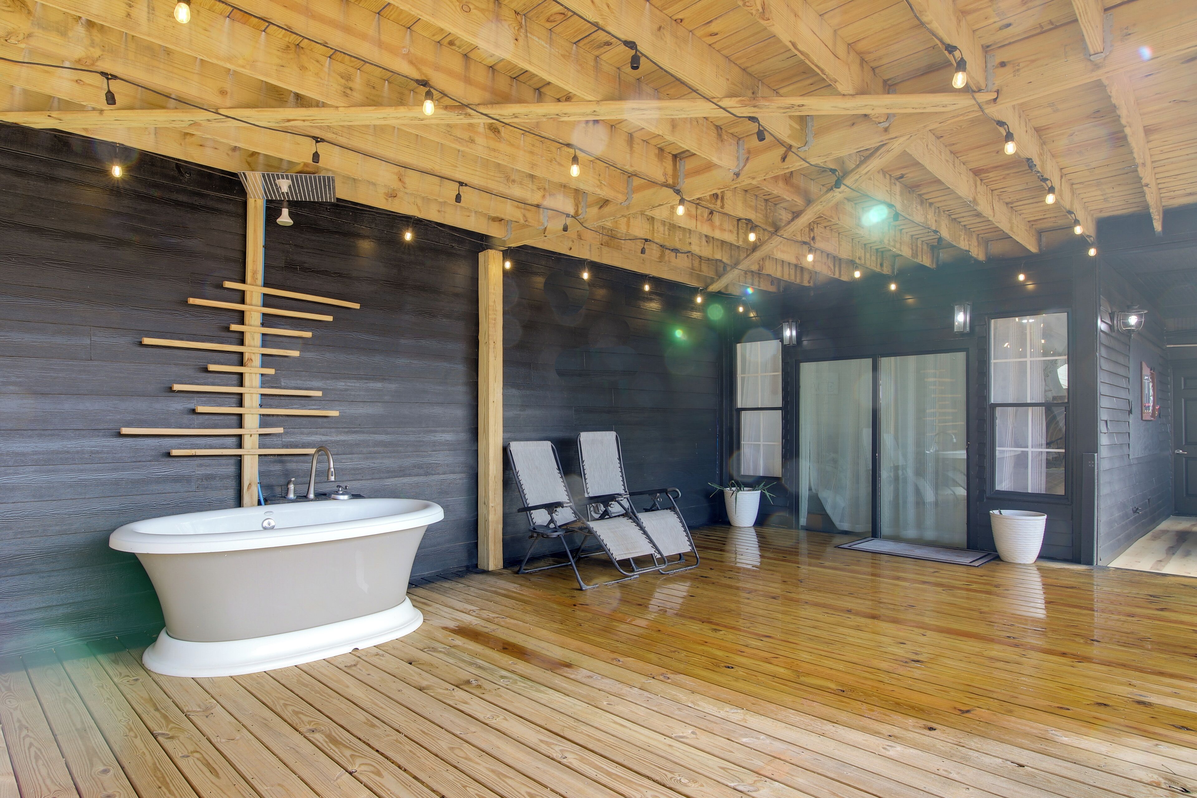 A modern bathroom with a freestanding bathtub, two lounge chairs, and a wooden ceiling.